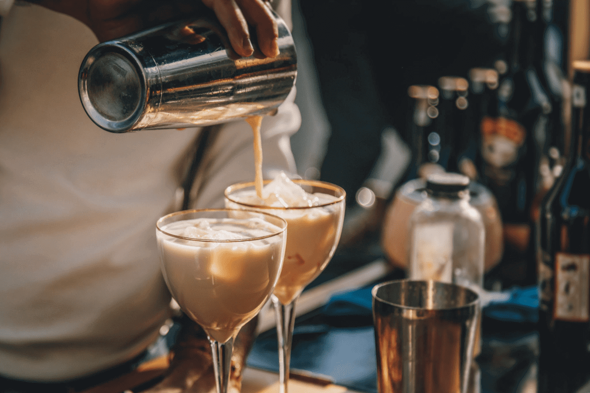 Bartender pouring cocktails into two glasses.