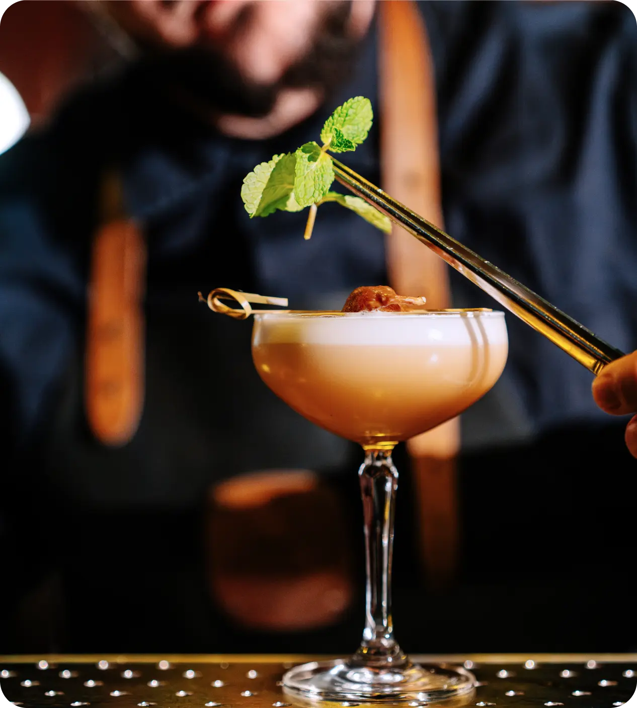 A bartender garnishing a cocktail with fresh herbs using tweezers.