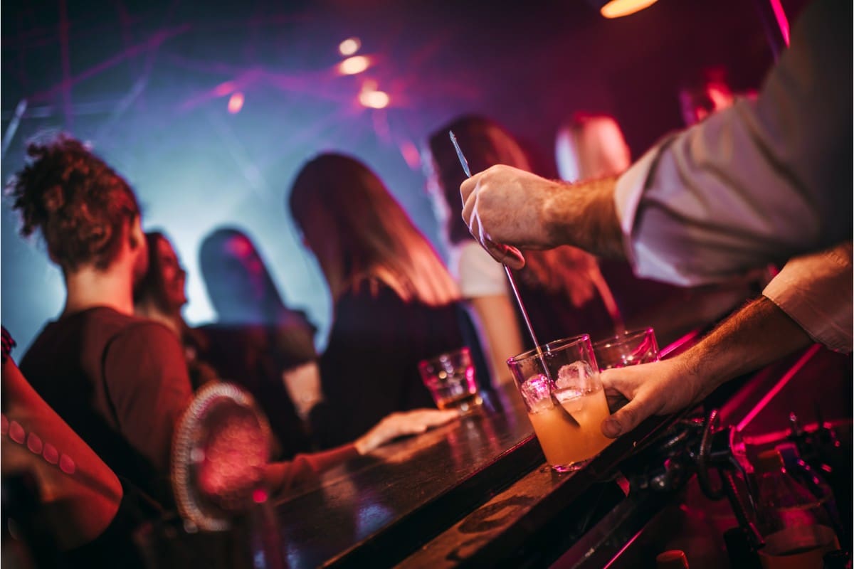 Bartender preparing a cocktail in a lively bar with patrons.