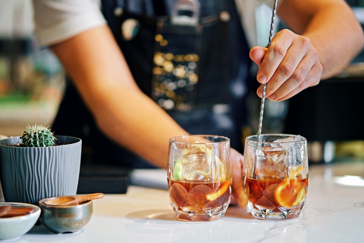 Bartender stirring two cocktails in glasses with ice and citrus.