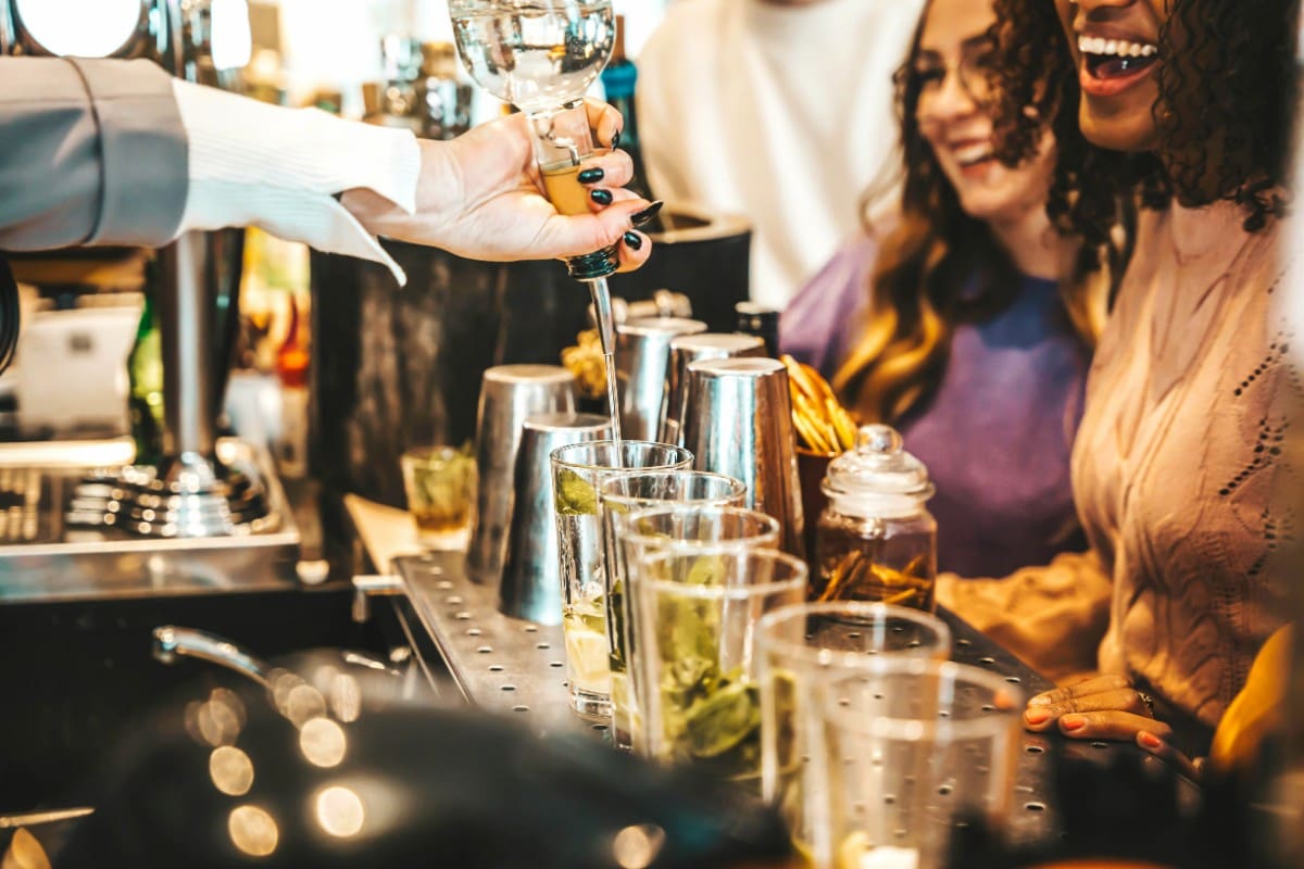 Bartender pouring a drink for a smiling woman at a bar.