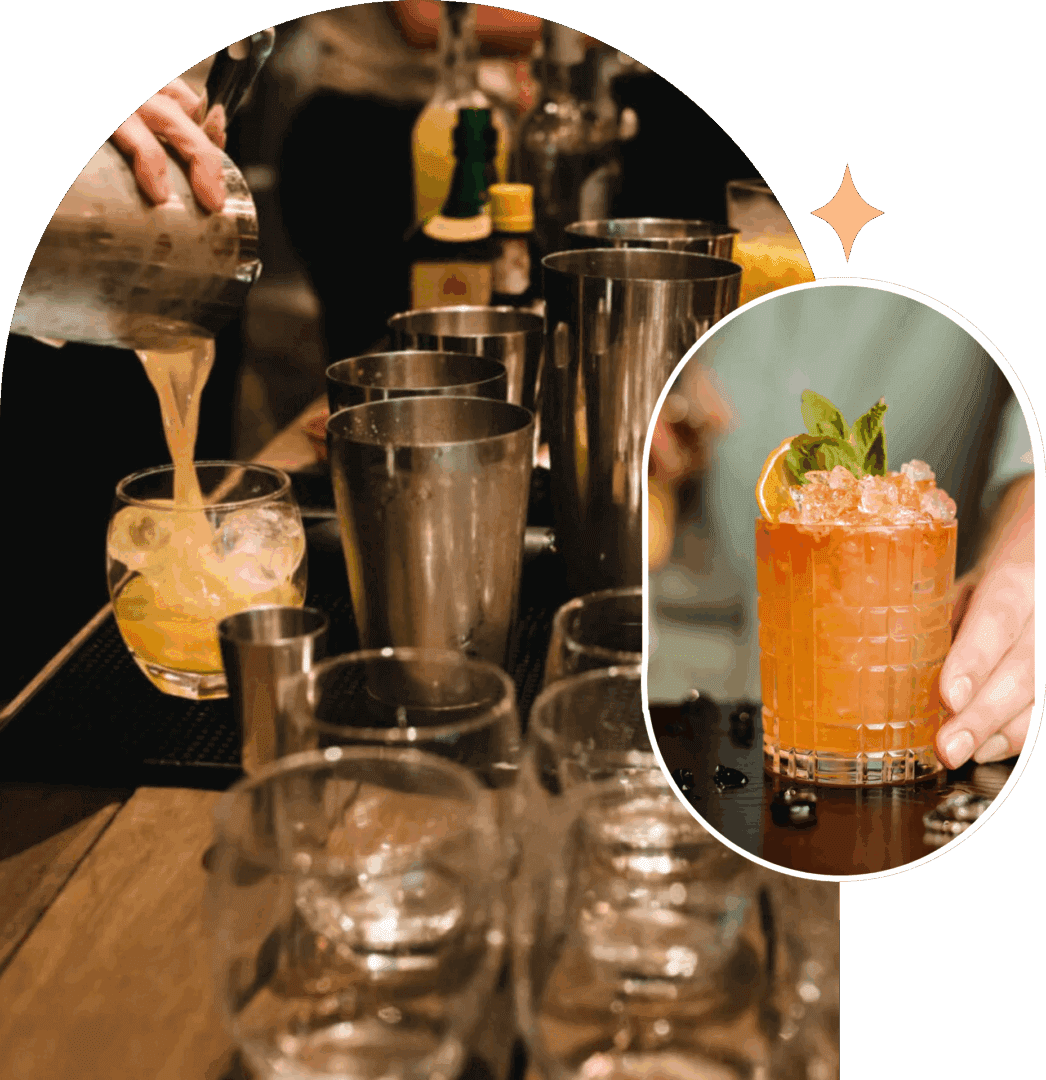 Two cocktails on a bar counter with bartenders in the background.