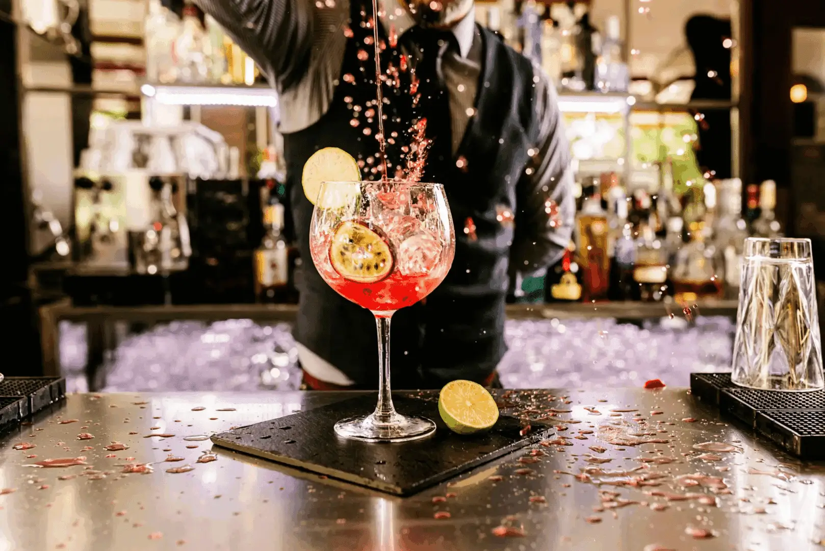 A splash of a red cocktail with lime garnish in a glass on a bar counter.